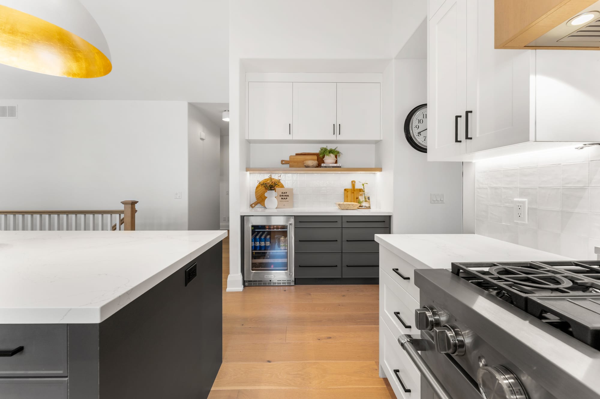 Beverage bar with glass-front wine fridge, lit floating shelf and grey cabinetry beside the commercial-style gas range