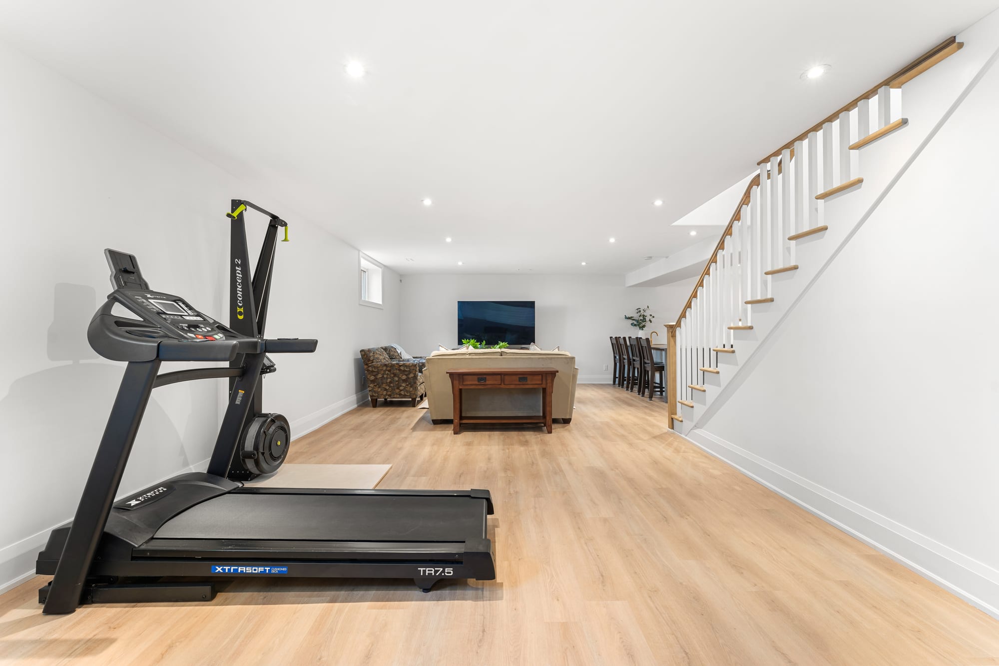 Lower-level home gym area with treadmill and rower, opening onto the recreation room