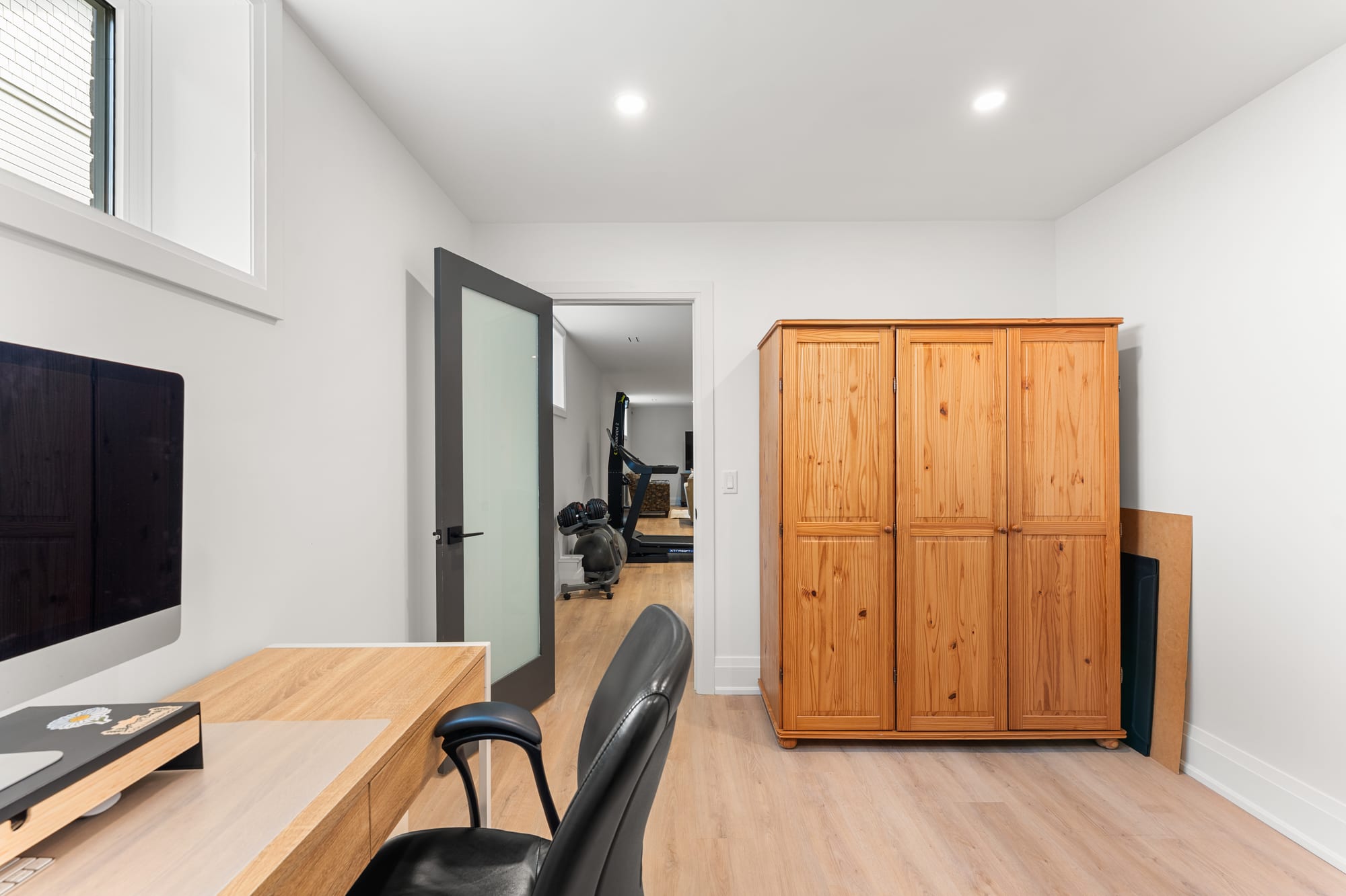 Lower-level home office with a built-in oak desk and pine wardrobe, looking through to the gym