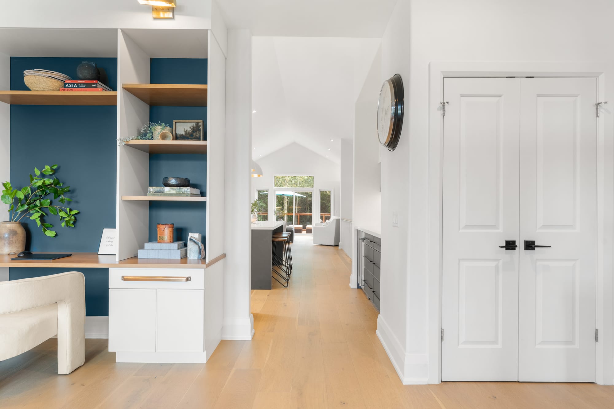 Hallway looking from the built-in office nook toward the kitchen, with wide-plank oak flooring and vaulted ceilings beyond